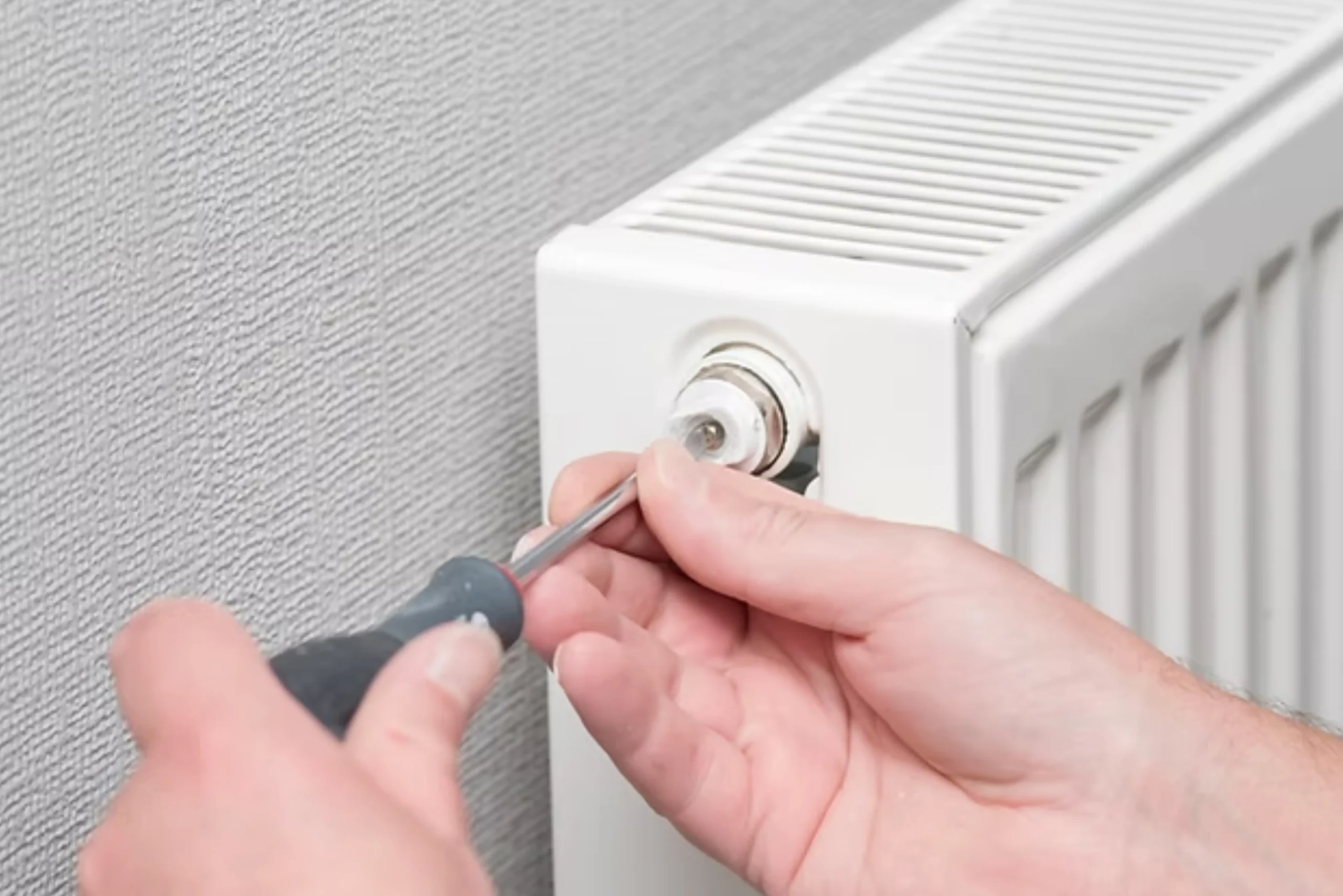 Electrician installing a white electric radiator with a screwdriver